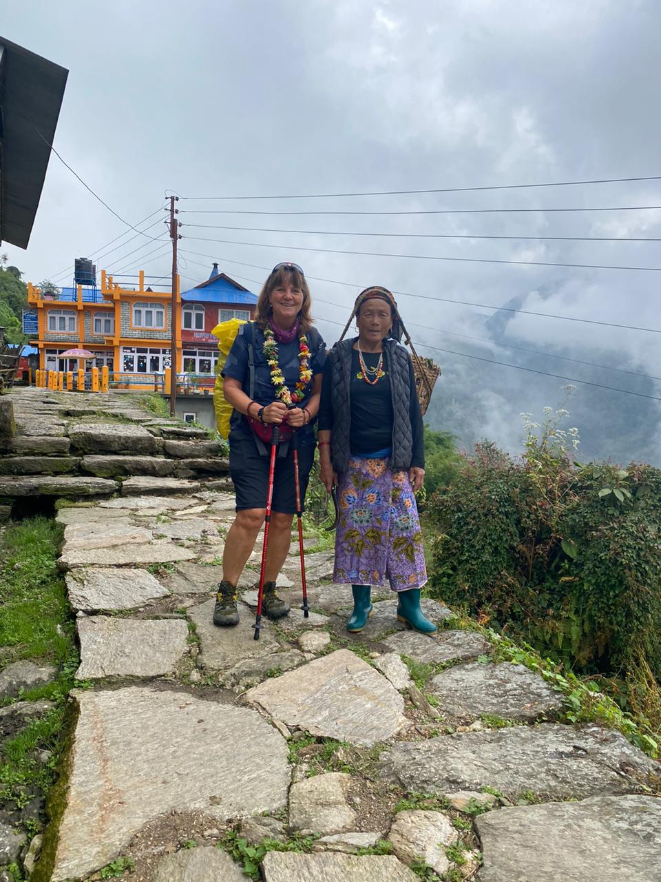 Two women standing on a stone path, one in trekking gear and another in traditional clothing.